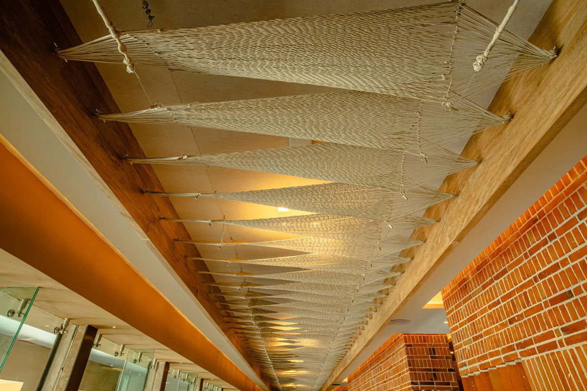 Lengthwise view of the CHI Xcaret ceiling, with pale woven panels suspended between timber beams.