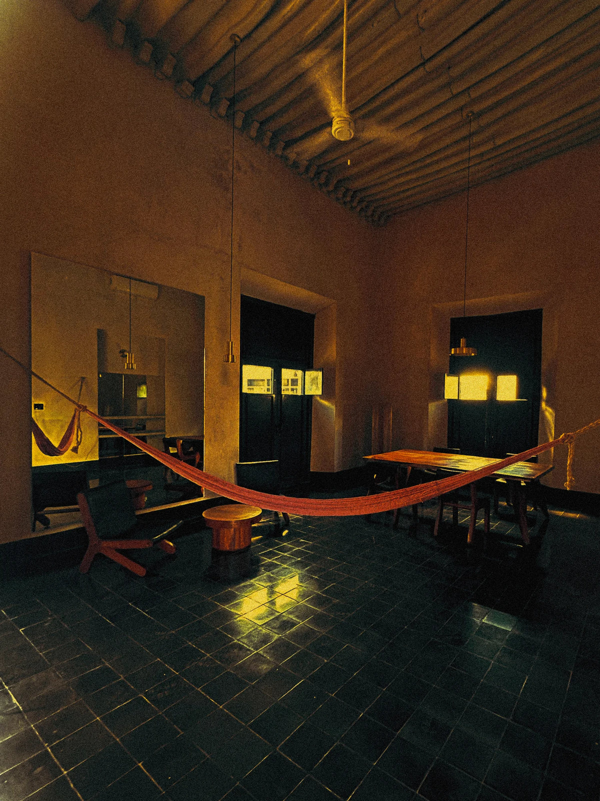 An orange hammock in a suite with warm walls, wooden beams and a green tiled floor.
