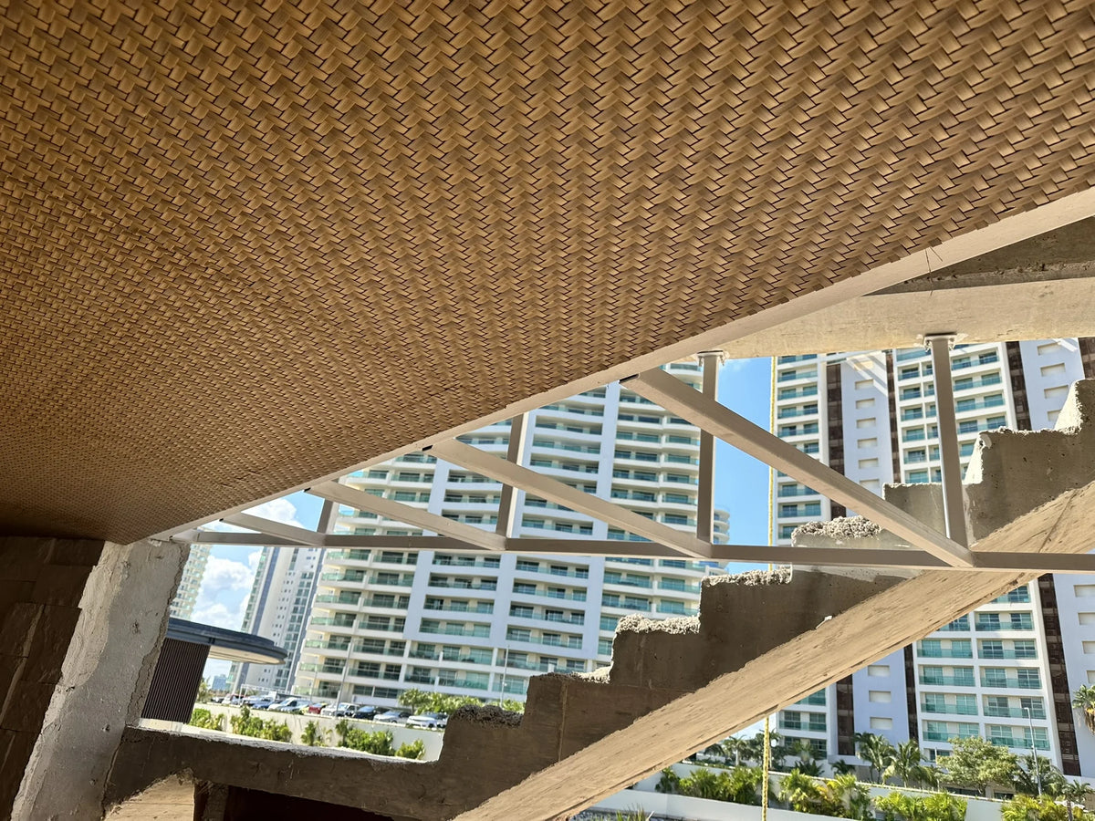 Detail of the woven ceiling during installation, beside a white structure and a concrete staircase.
