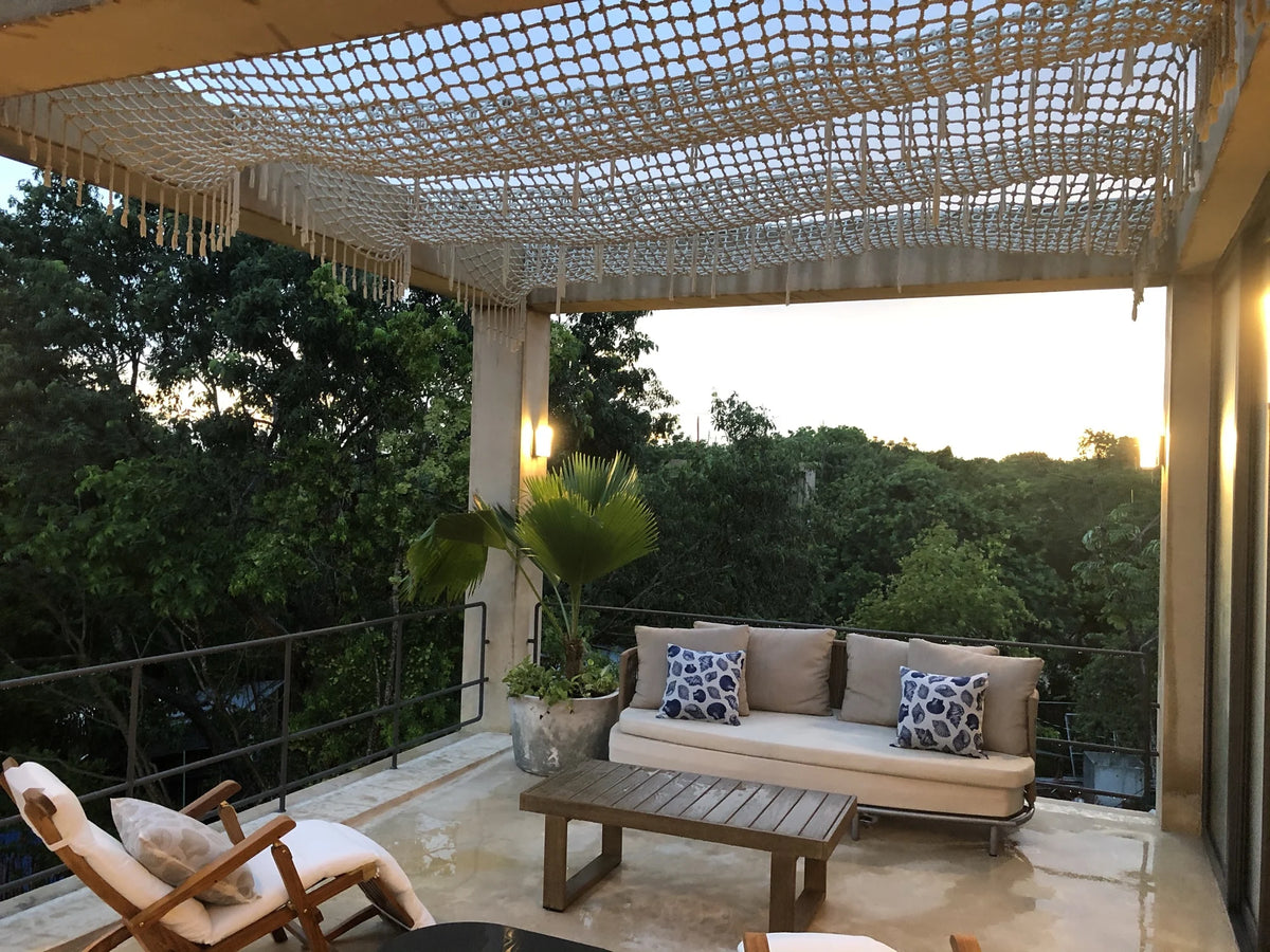 A wide view of the terrace with a sofa, wooden chairs and a woven canopy lit at dusk.
