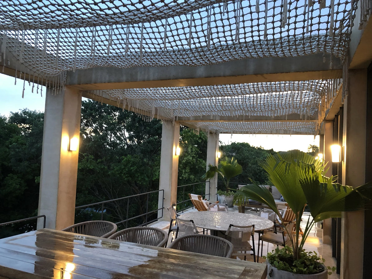 A long view beneath the terrace’s pale net canopy, with warm lights and greenery in the background.