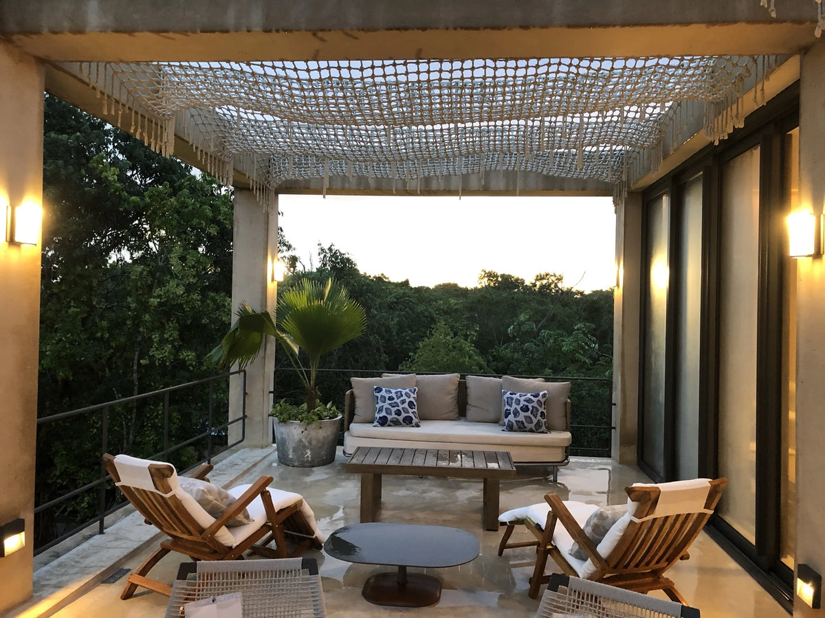 A sofa and chairs beneath a woven pergola on a terrace surrounded by greenery.