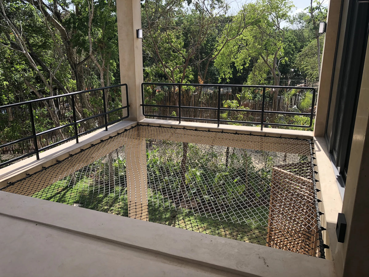 A pale net installed in a double-height space opening towards trees and greenery.