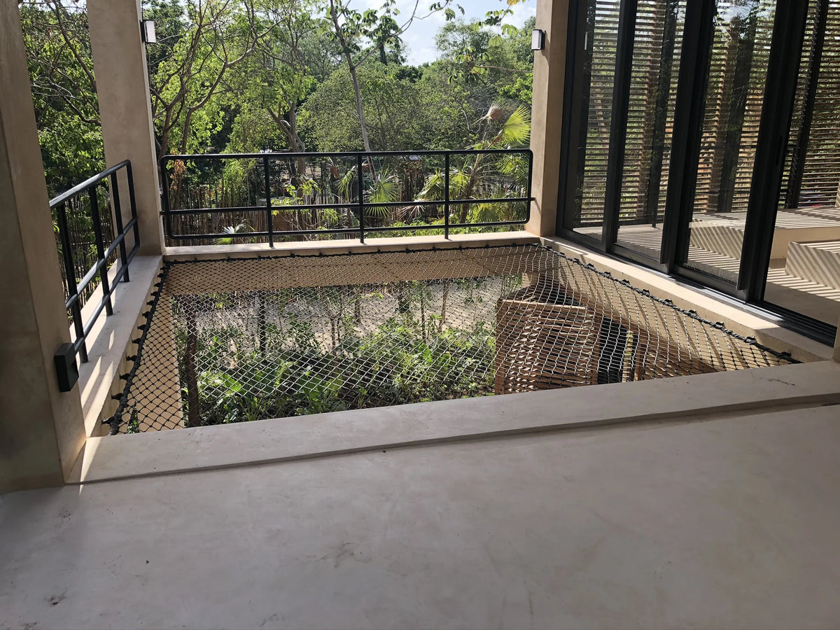 A view of an indoor net beside windows and black railings, with greenery outside.