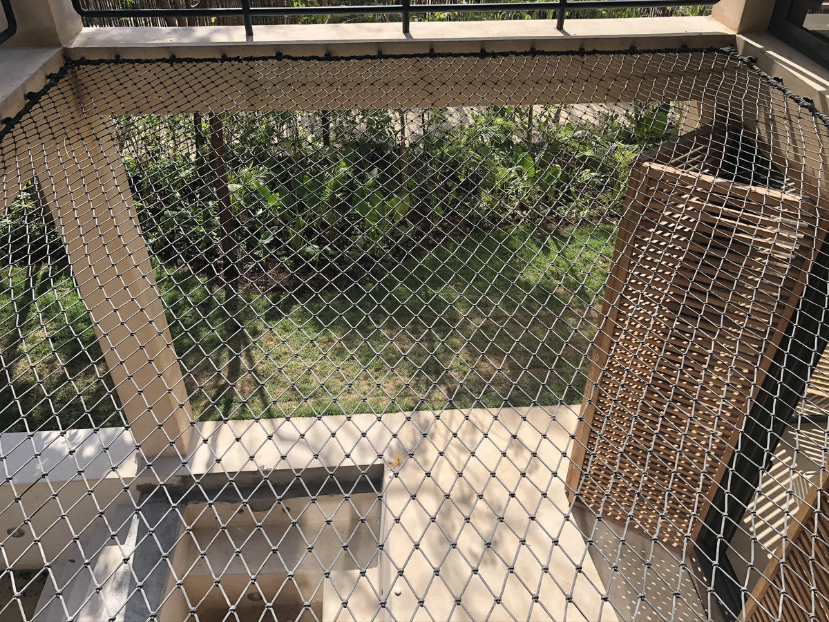 Detail of a tensioned net in a double-height space, with columns and trees visible through the weave.