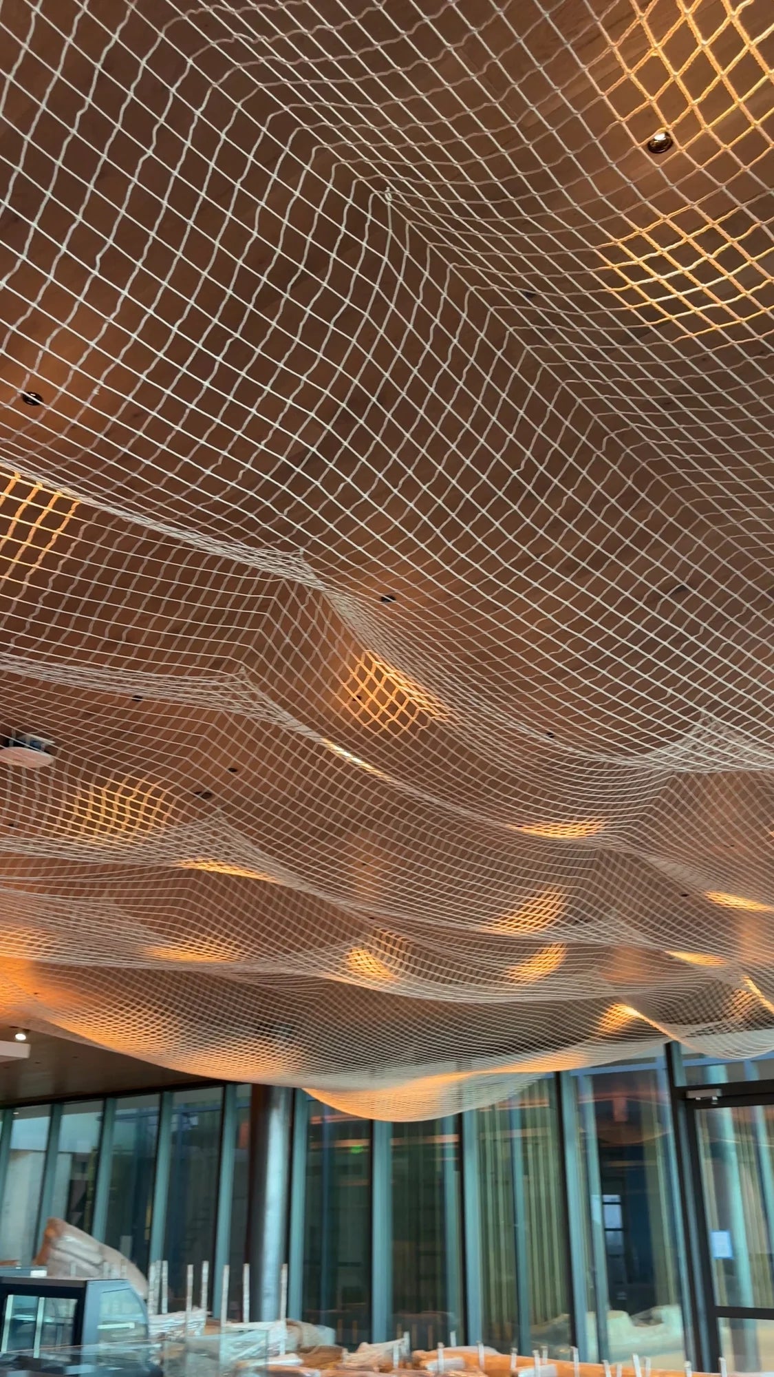 Pale net suspended in waves beneath a timber ceiling with warm lighting; protected furniture is visible below.