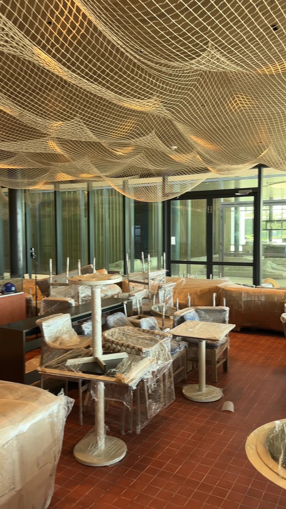 View of the room with suspended nets above tables and seating still wrapped in protective coverings.
