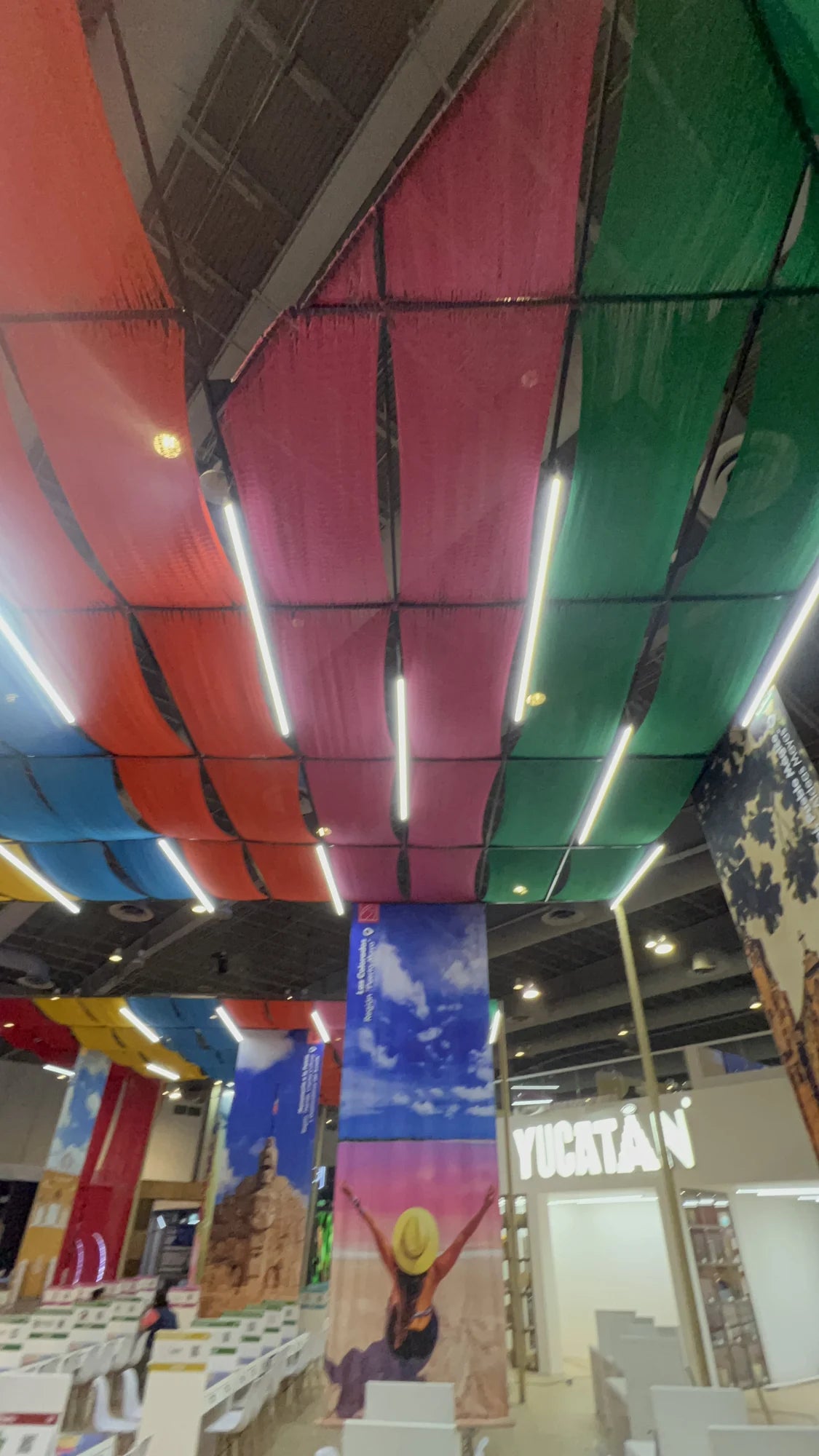 View from inside the Yucatán stand, with green, pink, orange and blue woven bands suspended above the meeting areas.