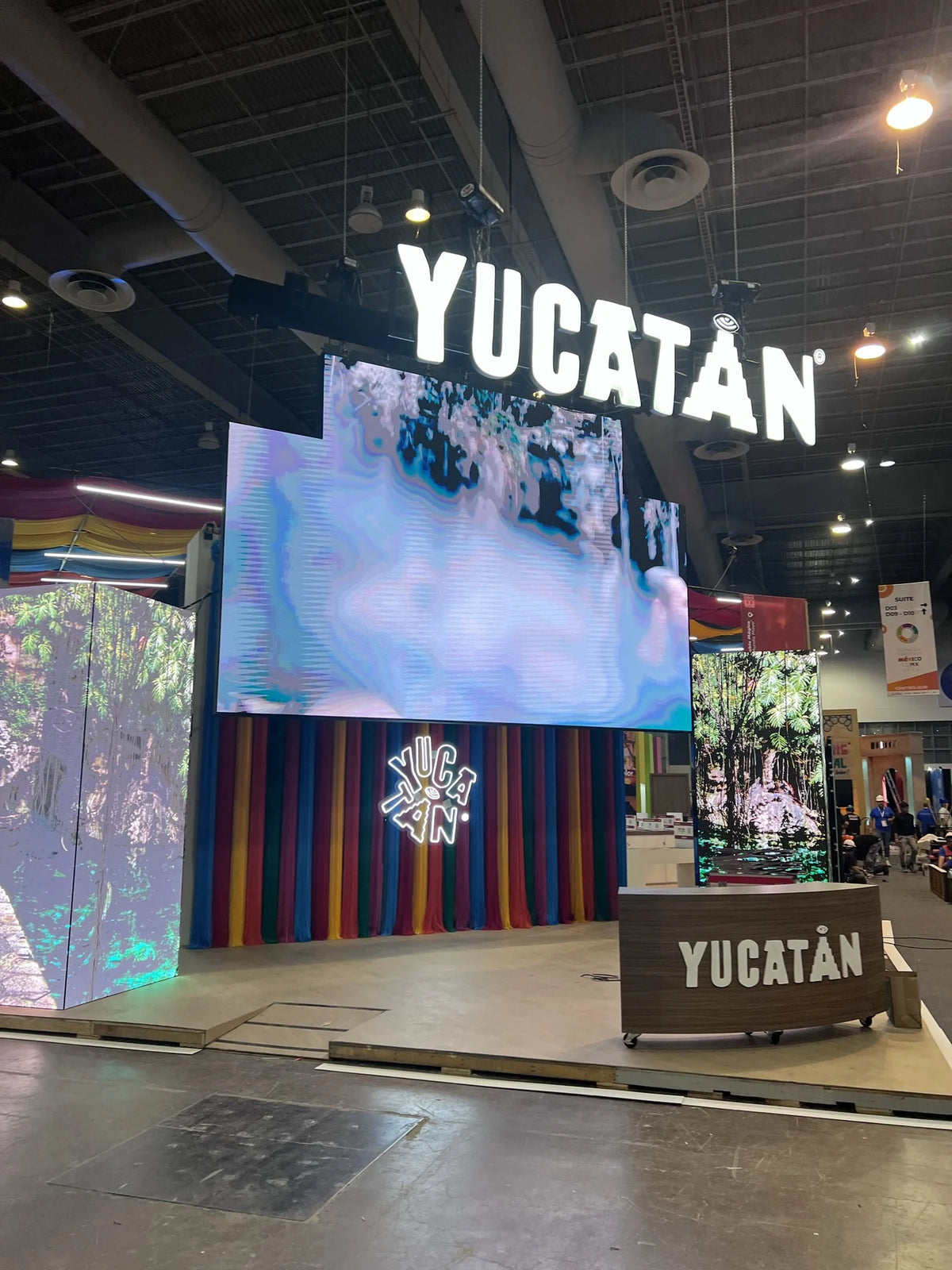 Front of the Yucatán stand, with multicoloured thread curtains beneath a screen and an illuminated sign.