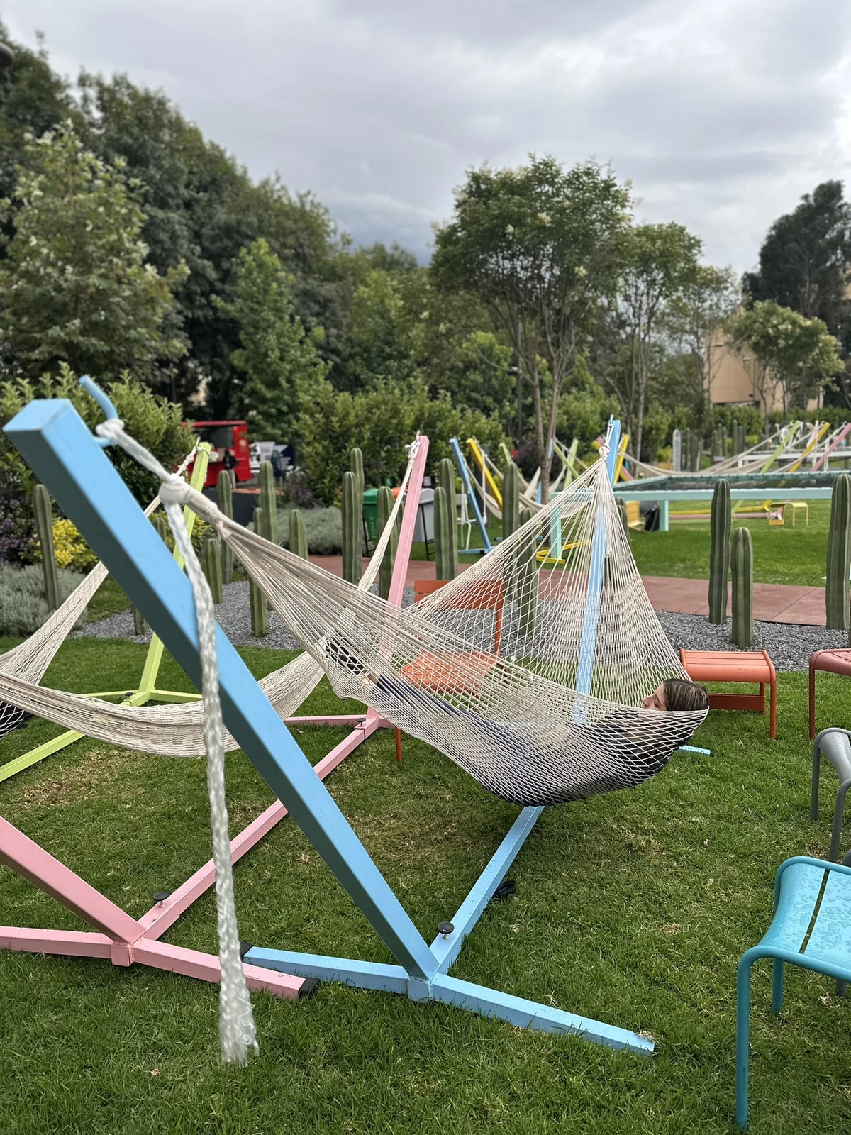 A hammock on a blue stand with other colourful hammocks among the campus trees.