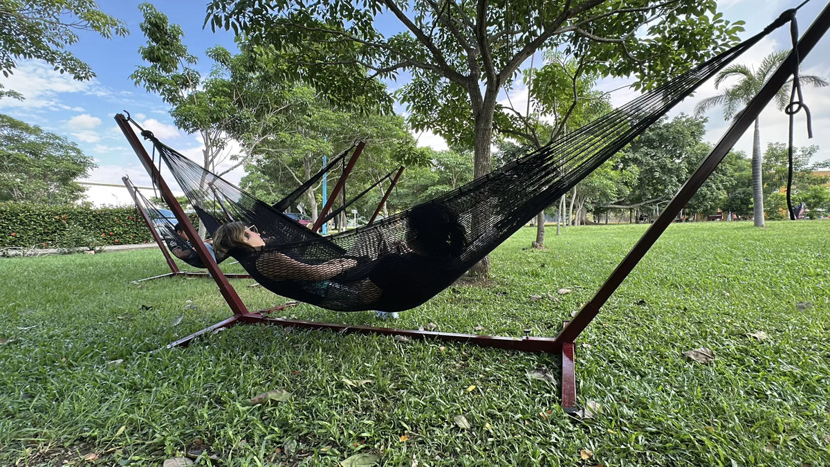 A person resting in a dark hammock above the campus lawn beneath the trees.