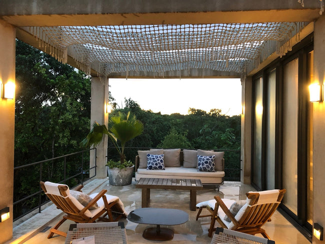 Salon extérieur sous une pergola tissée, éclairé à la tombée du jour à Playa del Carmen.