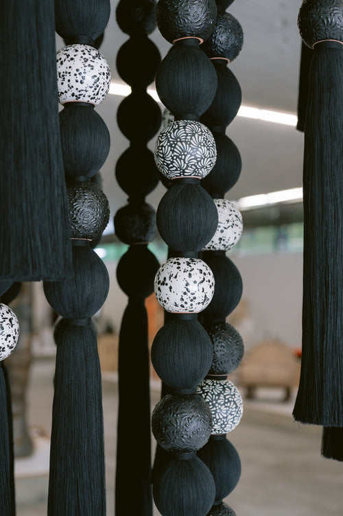Detalle de FILAMENTO: hilos negros junto a piezas cerámicas decoradas en blanco y negro.