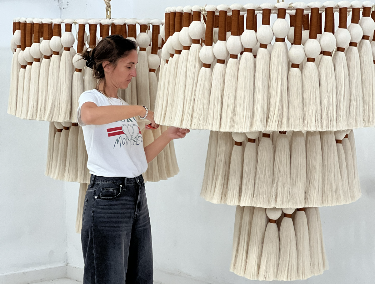 Manos anudando hilo verde en un bastidor de madera durante la elaboración de una pieza textil.